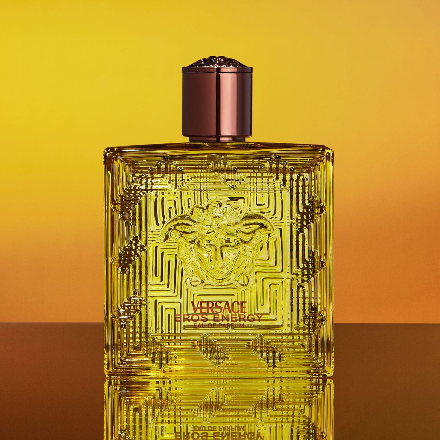 Versace Eros Energie perfume bottle on a gradient yellow and orange background