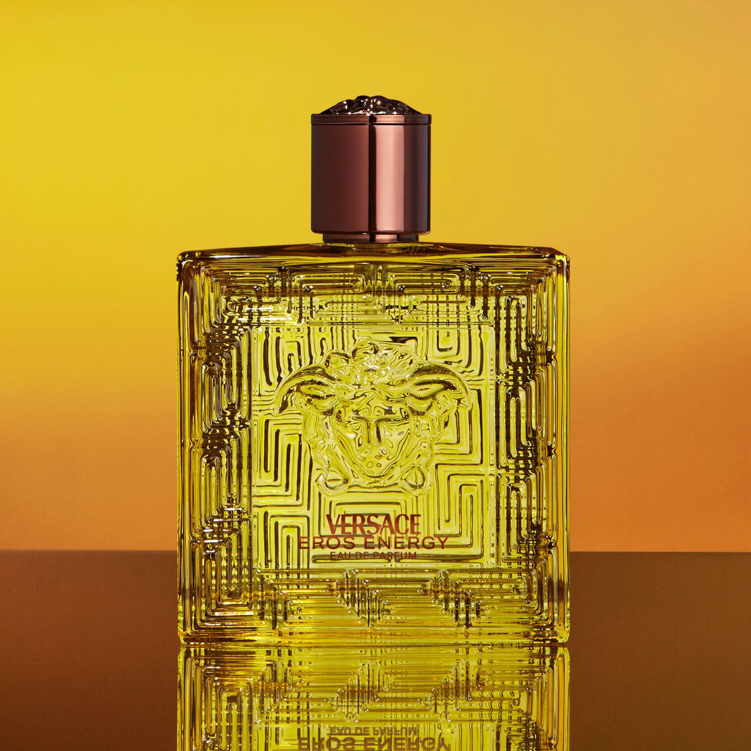 Versace Eros Energie perfume bottle on a gradient yellow and orange background